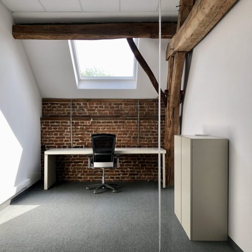 Een minimalistisch kantoor met bakstenen muur, wit bureau, bureaustoel, dakraam en zichtbare houten balken.